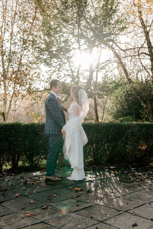 Newlyweds lovingly exchange glances during an outdoor golden hour portrait session against a backdrop of autumn trees and foliage.