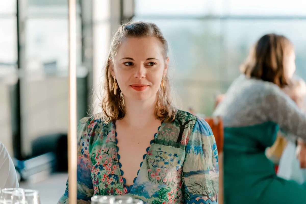 A wedding guest sits at the reception wearing a colourful floral print V-neck dress and statement earrings, captured in natural light during a candid moment.