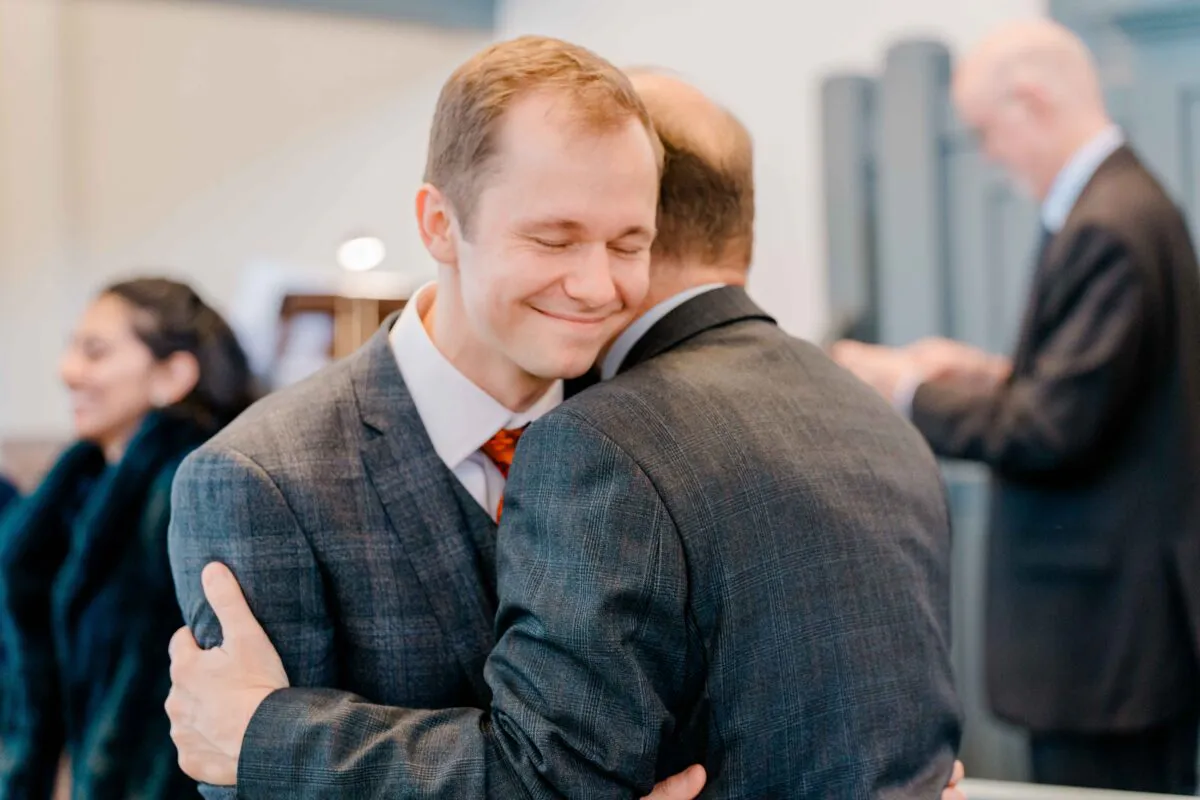 A groom shares a warm, emotional embrace with a guest during a heartfelt wedding celebration moment.