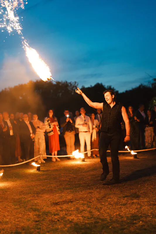 A skilled fire performer entertains wedding guests gathered outside during dusk under a clear blue evening sky.