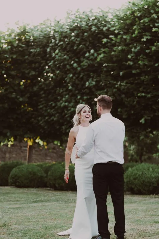A newlywed couple laughing joyfully together outdoors in a manicured garden setting during their wedding celebration.