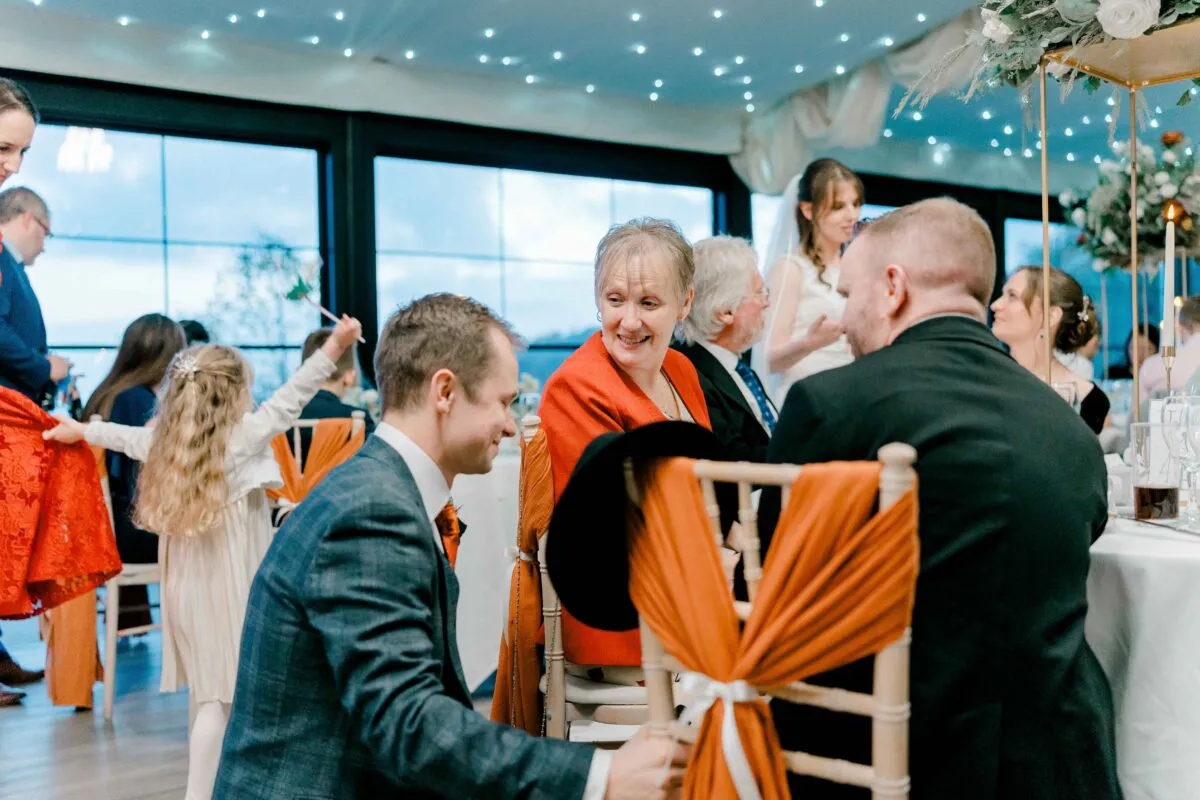 Guests enjoy lively conversation around a decorated table during the wedding breakfast under a twinkling fairy light ceiling canopy.