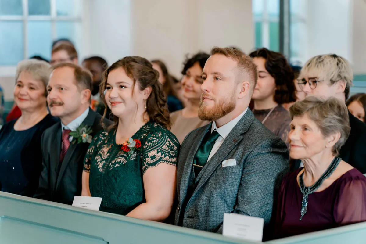 A candid shot of wedding guests seated in a church pew, watching the ceremony with gentle smiles.