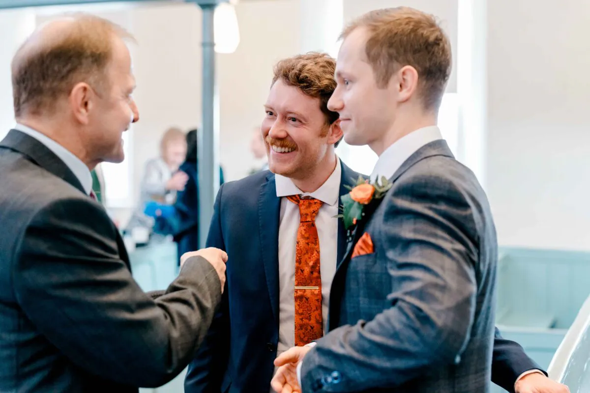 A smiling groom and a guest share a cheerful moment and a handshake during the wedding reception.