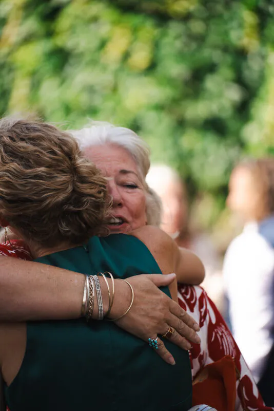 An older woman shares a tender, emotional embrace with a guest outdoors during a wedding celebration.