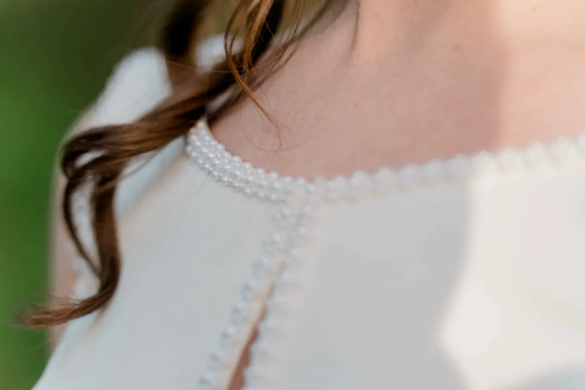 A close-up detail shot highlights the intricate pearl-beaded neckline and keyhole detail of a white wedding dress.
