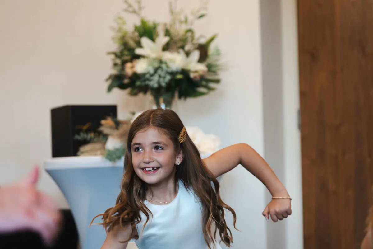 A young flower girl smiling happily during the wedding celebration with a floral arrangement visible in the background.