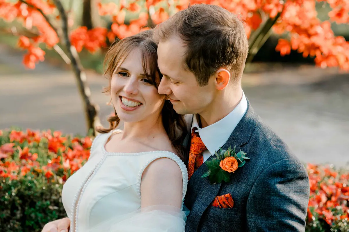 A smiling bride and groom embrace outdoors surrounded by vibrant autumn foliage during golden hour portraits on their wedding day.