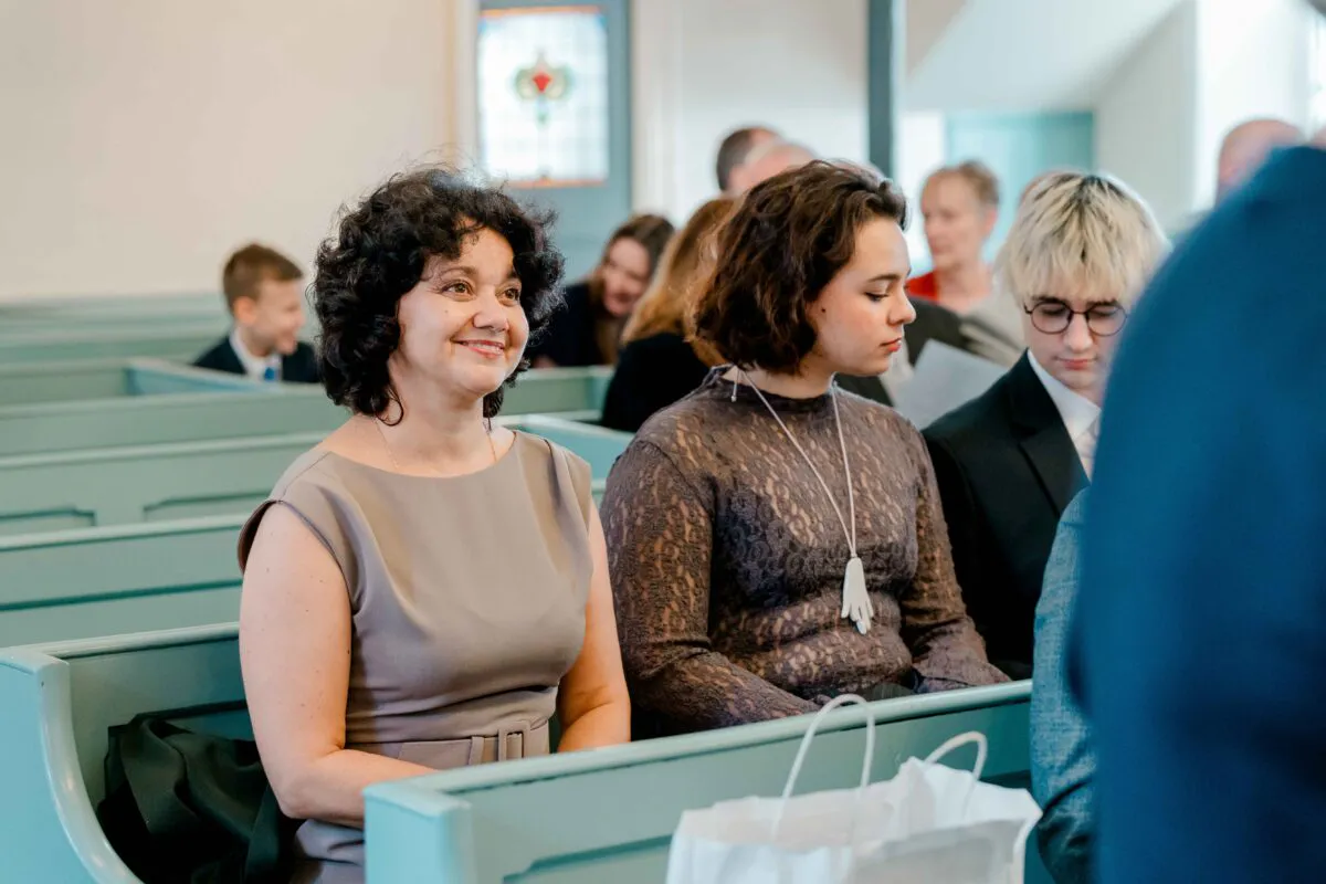 Wedding guests seated in pale green church pews, with a smiling woman in the foreground looking towards the ceremony.