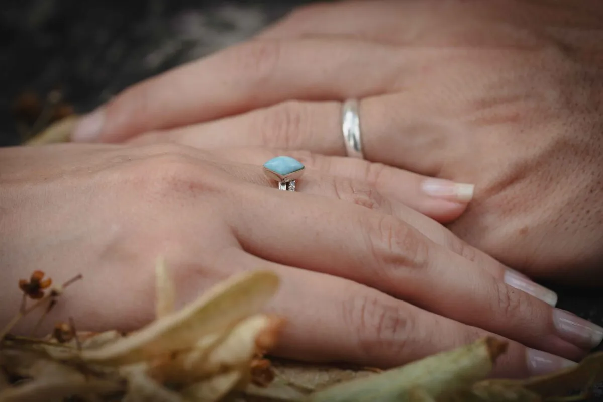 Close-up macro shot of a couple holding hands, showcasing an engagement ring with a light blue stone and a simple silver wedding band.