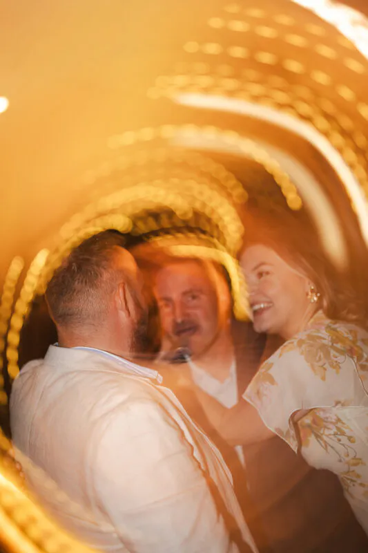 A joyous couple shares a lively moment under warm glowing lights during a vibrant evening wedding reception.