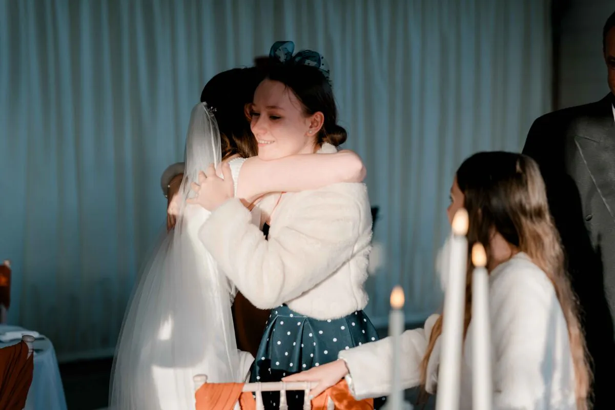 A guest warmly embraces the bride in a tender moment while another guest watches nearby at the wedding reception.
