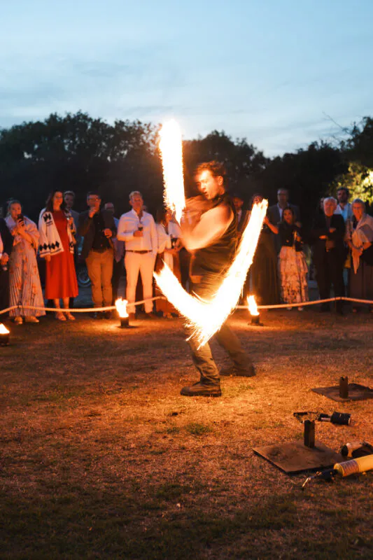 A skilled fire performer captivates an audience of wedding guests outside during the evening reception with a dynamic flame display.