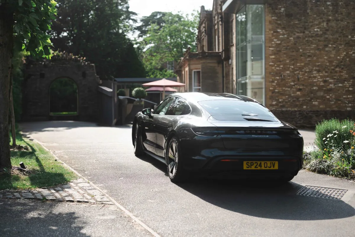 A sleek modern sports car parked on a paved driveway outside a traditional country house venue on a bright sunny day.