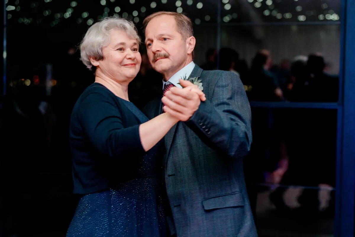 An older couple shares a tender dance together during the evening reception, surrounded by a soft bokeh of lights in the background.