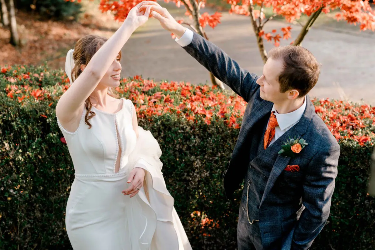 A bride and groom share a dance outdoors near vibrant red autumn foliage during the golden hour.