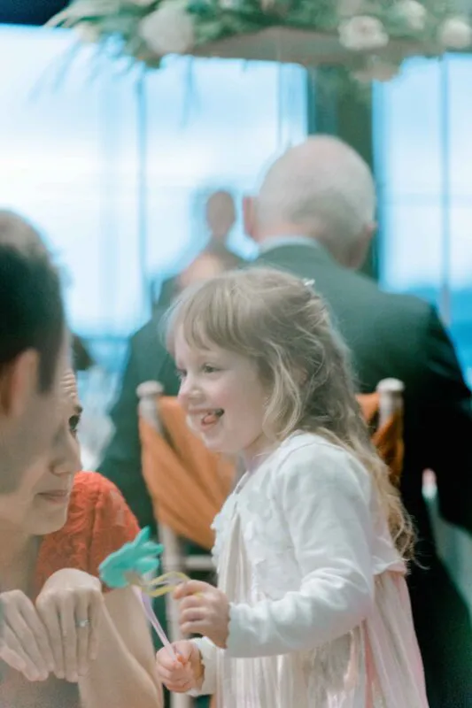 A young flower girl laughs joyfully while holding a small toy during the wedding reception.