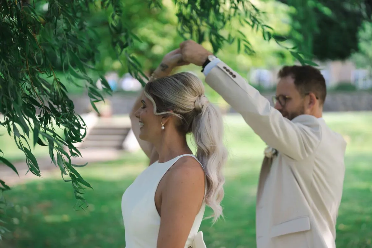 A newlywed couple shares a joyful dance outdoors under the draping branches of a willow tree.