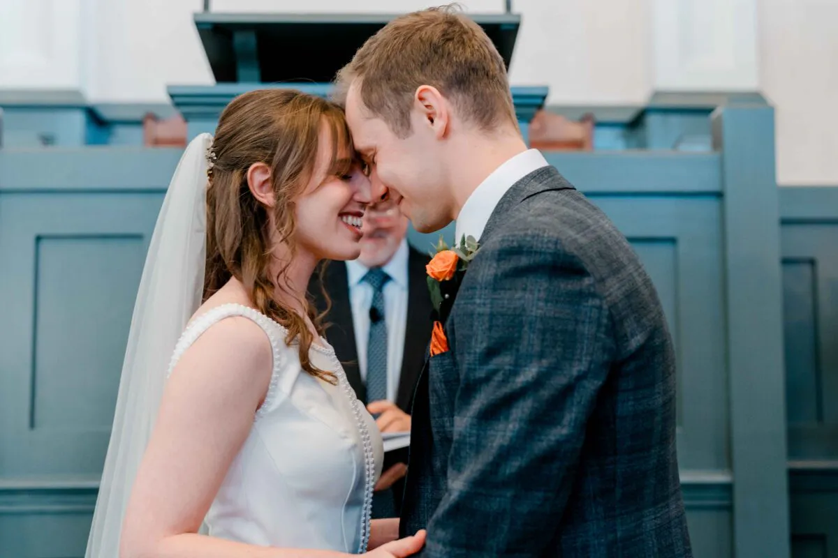 The bride and groom share a tender nose-to-nose moment smiling at the altar during their wedding ceremony.