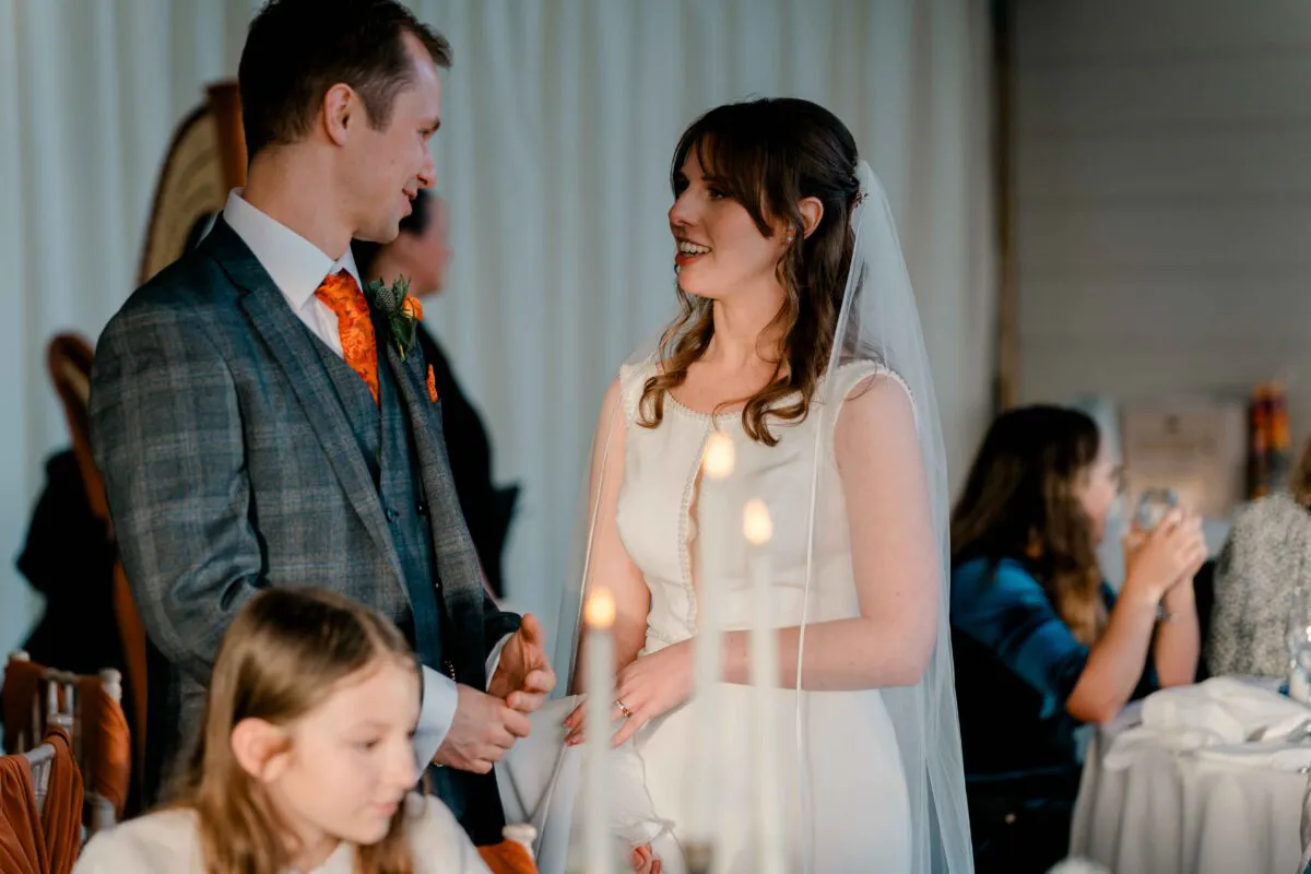 A smiling bride and groom share a joyful conversation during the wedding reception while seated at the top table.