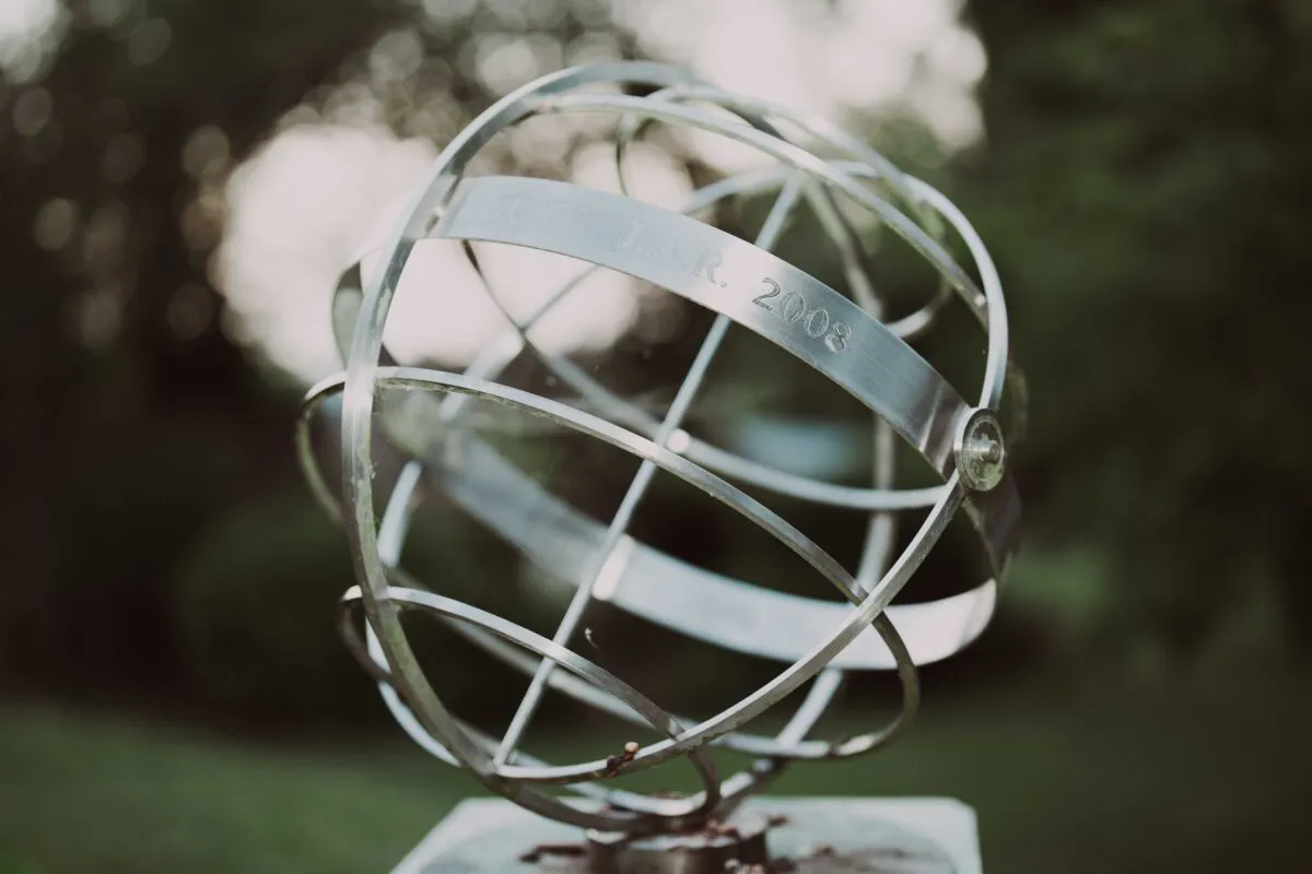 A close up shot of a metallic silver armillary sphere sculpture outdoors against a softly blurred green garden background.