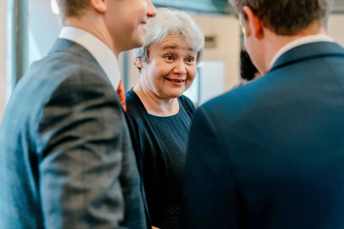 An older woman smiling warmly while chatting with guests during a wedding reception.