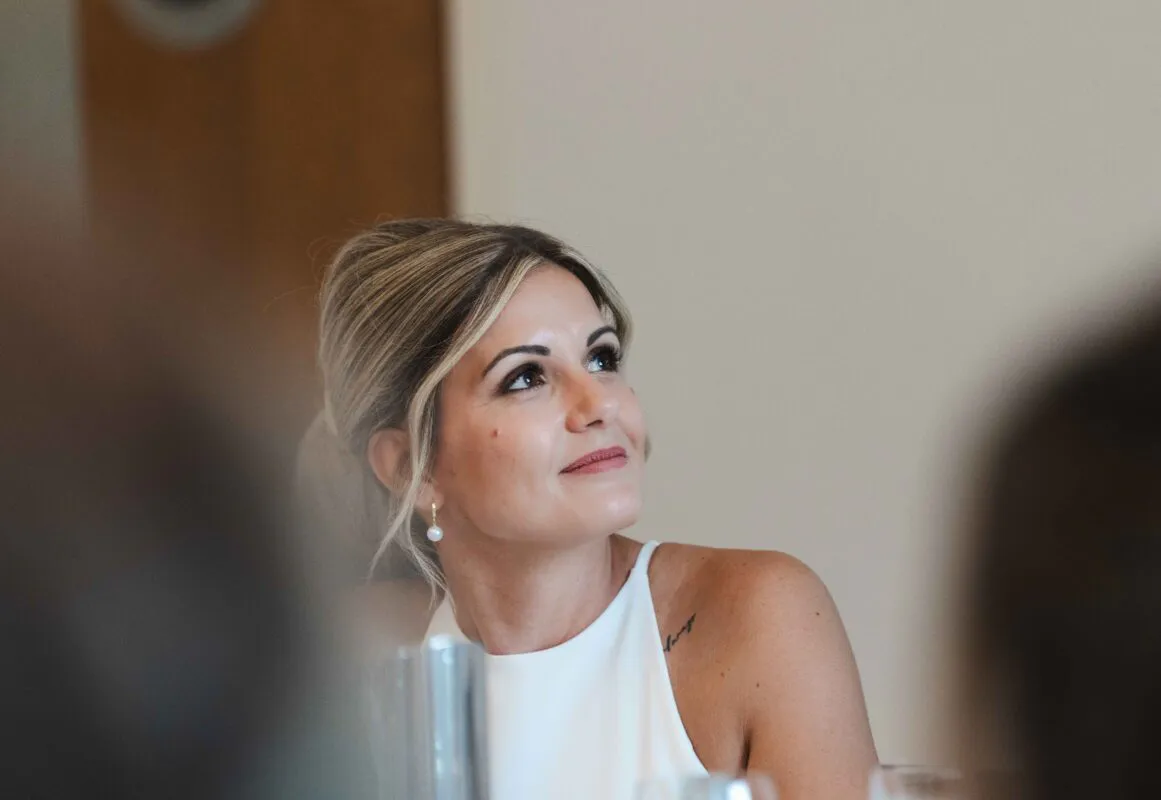 A candid portrait of a smiling bride with blonde hair in an updo and a white halter-neck dress, looking upwards and away.