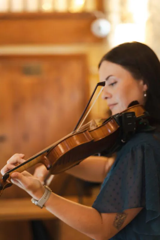 A musician plays the violin during a wedding ceremony, captured in a shallow depth of field with warm indoor lighting.