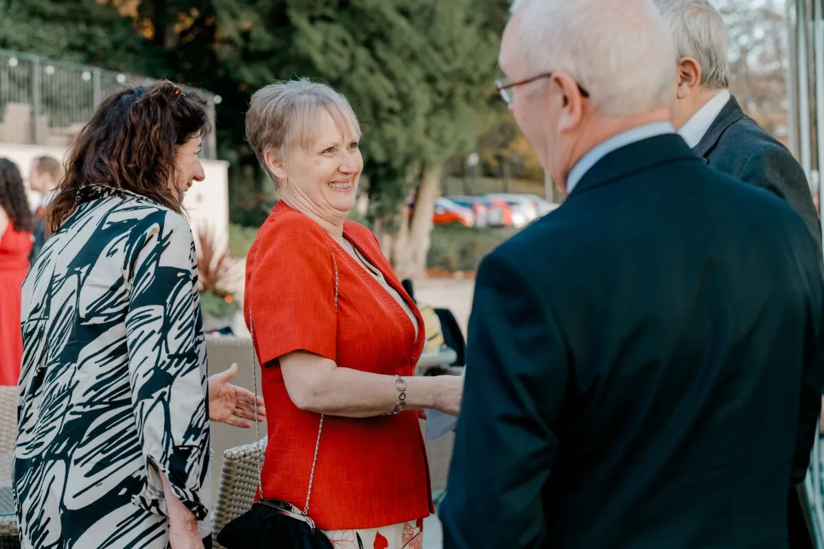 Wedding guests mingling and smiling outdoors during a reception under natural light.