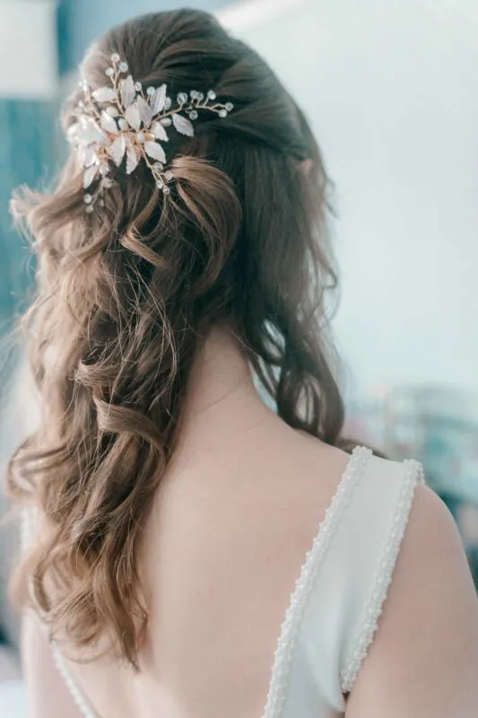 A close-up back view of a bride showcasing her half-up, half-down curly hairstyle adorned with an intricate gold and pearl hair comb.