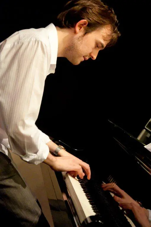 A musician plays the grand piano in a dimly lit venue, expertly pressing the keys during a live wedding performance.