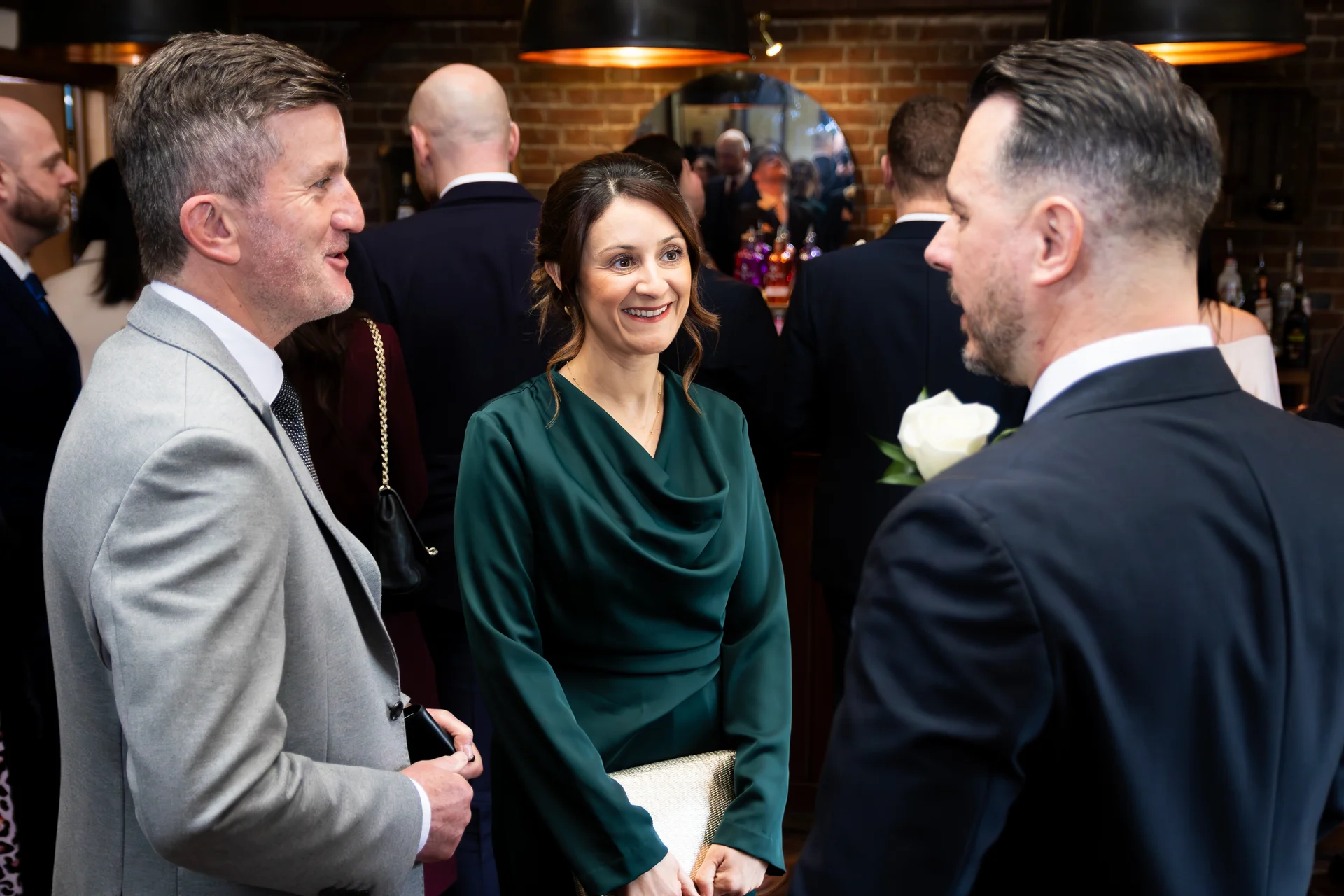 Wedding guests mingle and converse in a rustic pub venue with exposed brick walls during the drinks reception.