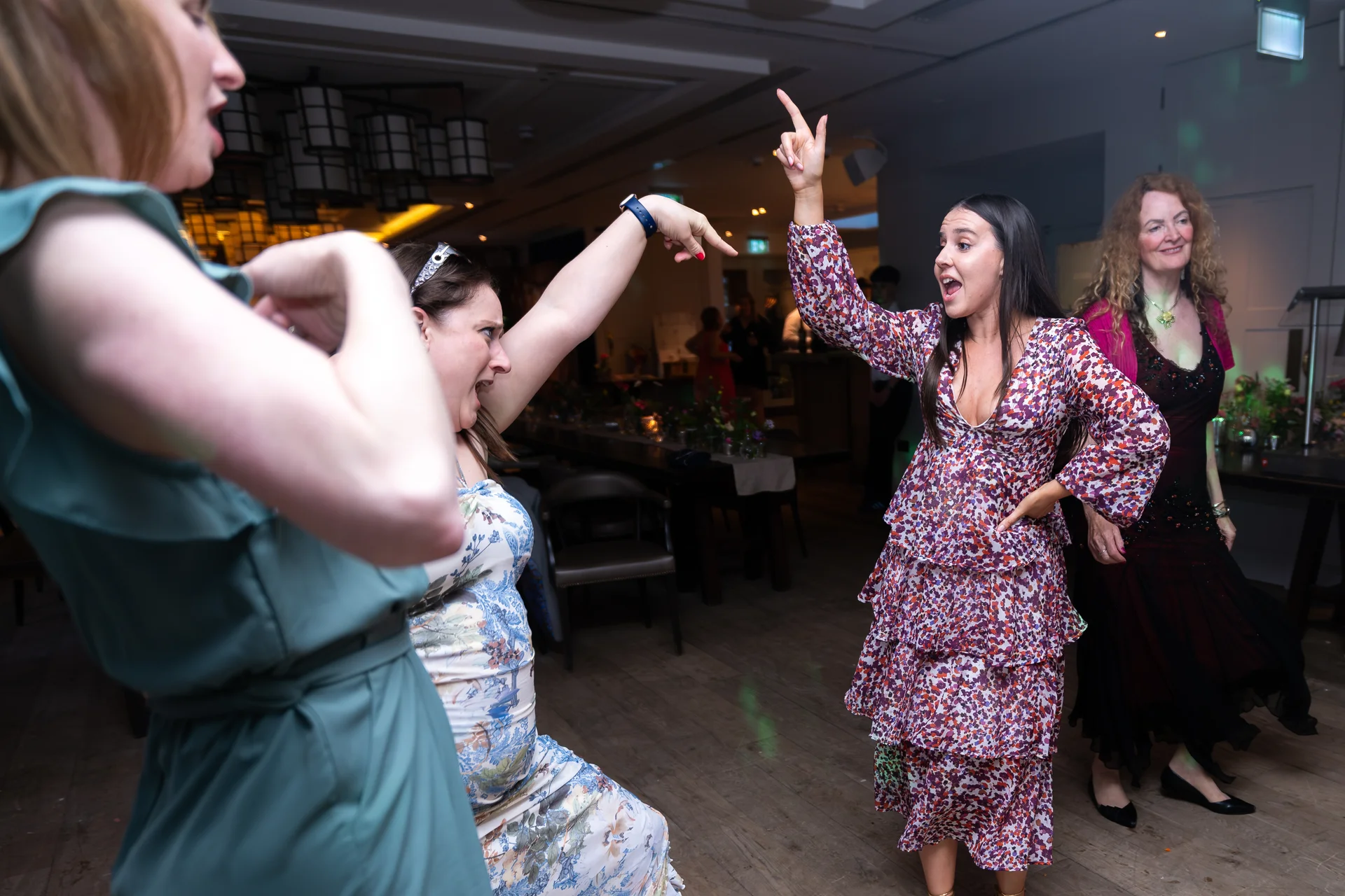Several wedding guests energetically dance and laugh together on the wooden dance floor during the evening reception.