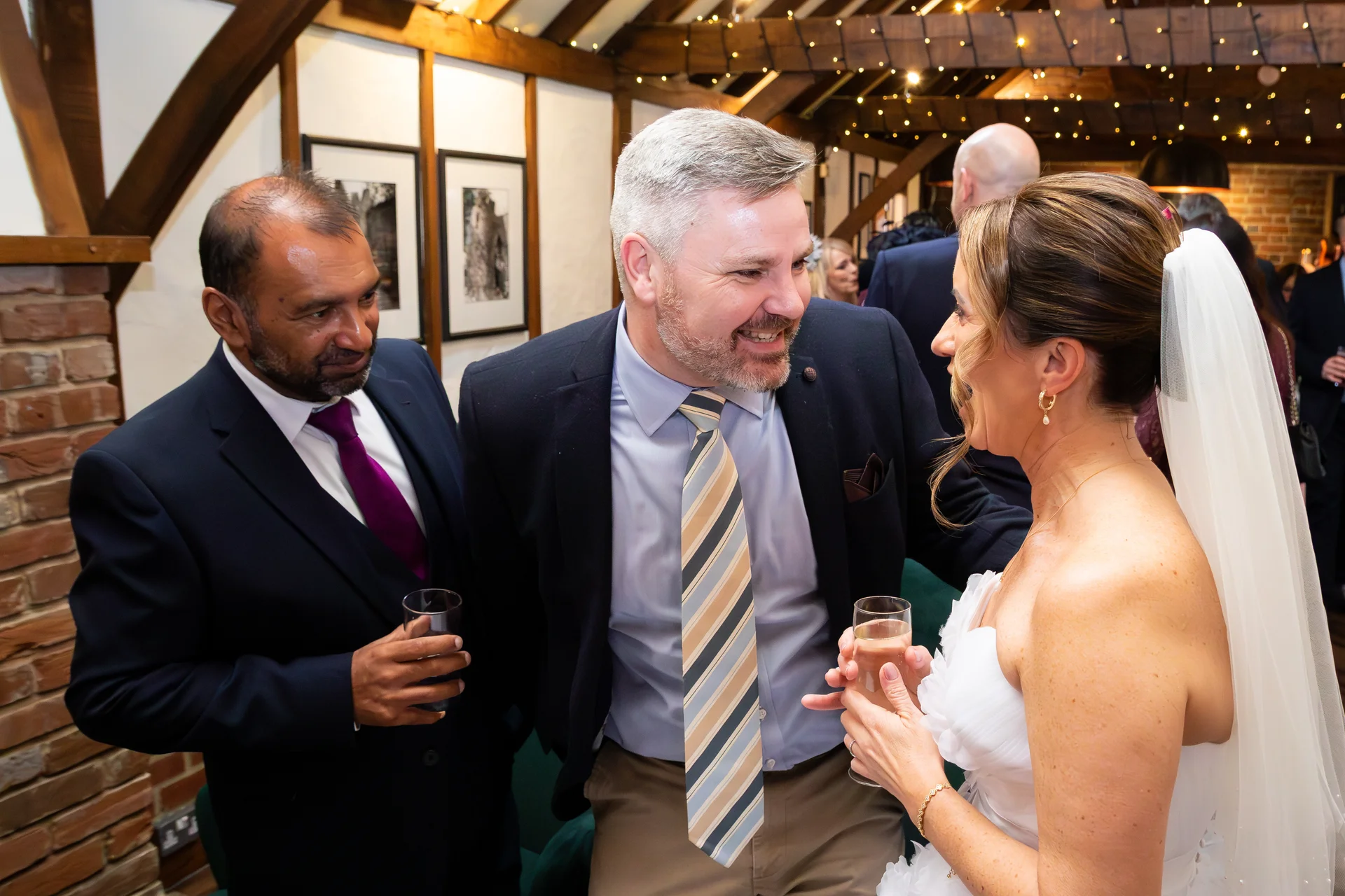 Guests and the bride mingle and share a joyful laugh during the drinks reception inside an atmospheric barn venue.