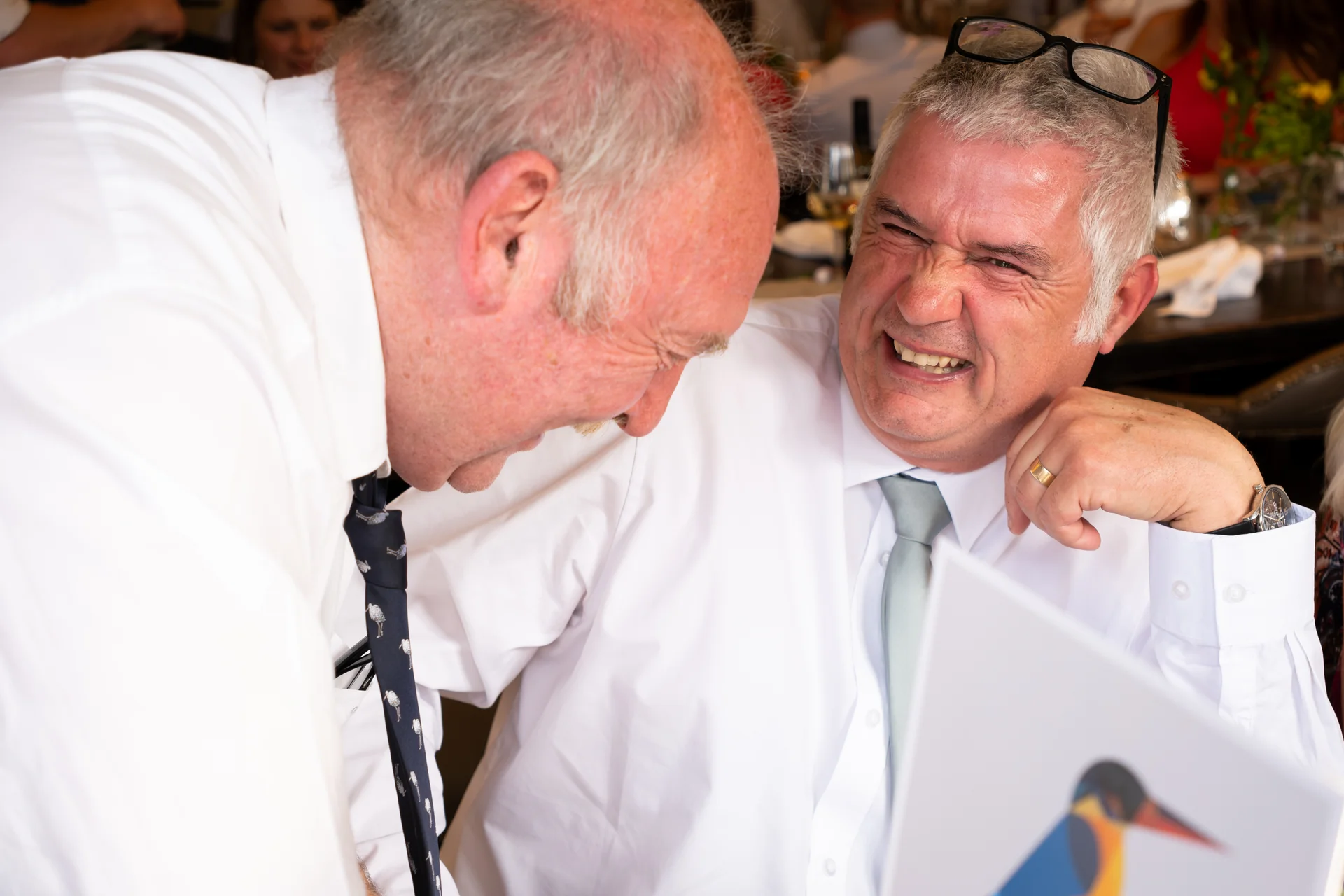 Two mature male wedding guests share a hearty laugh and a joyful moment together during the reception.