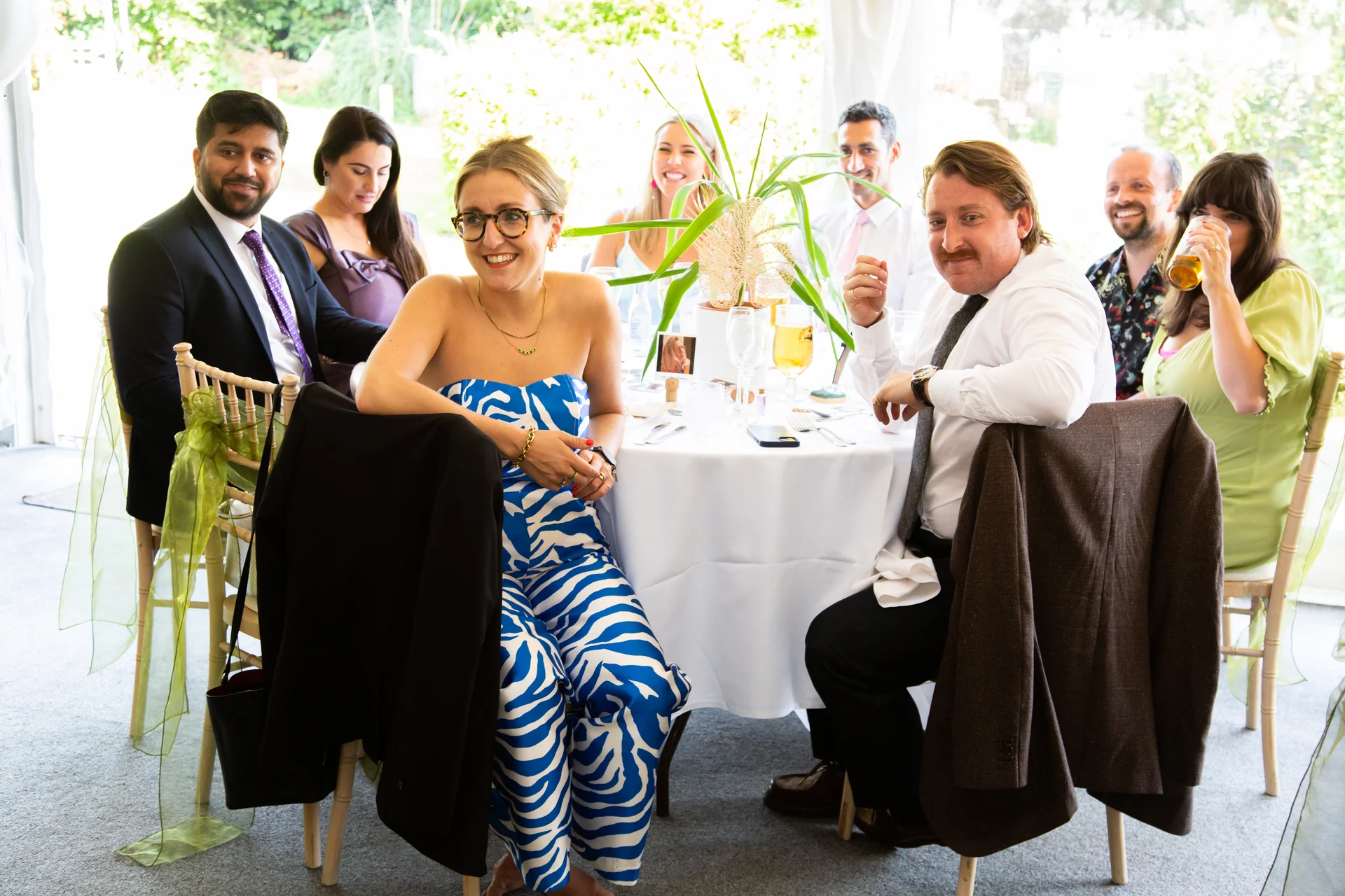 A candid group of wedding guests seated around a dining table, laughing and enjoying the wedding breakfast together.