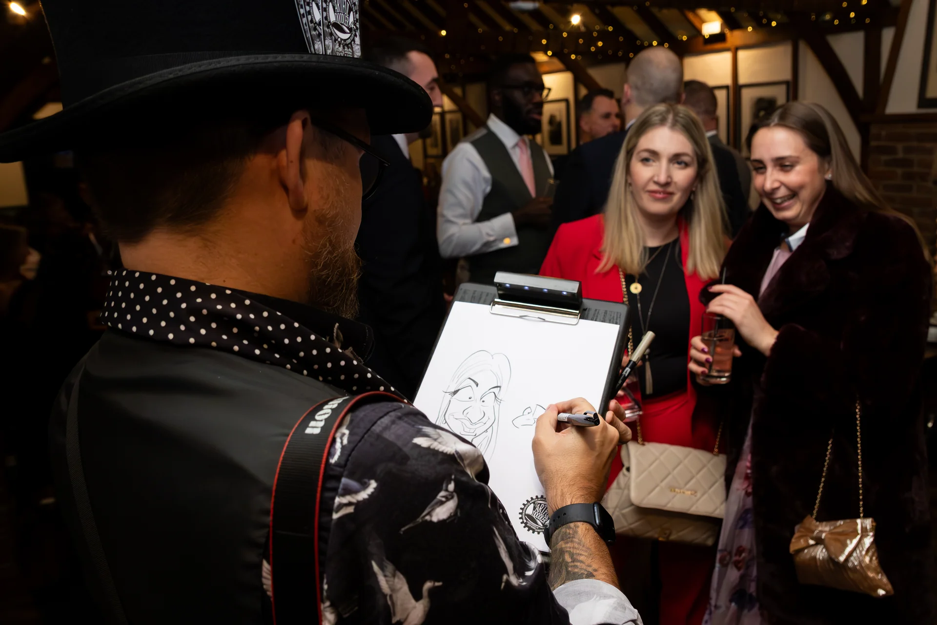 A live caricaturist sketches a laughing wedding guest on a clipboard while onlookers watch and smile during the evening reception.