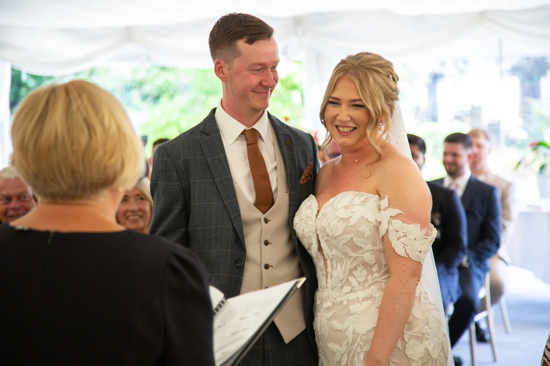 A joyful bride and groom share a happy moment laughing together during their marquee wedding ceremony.