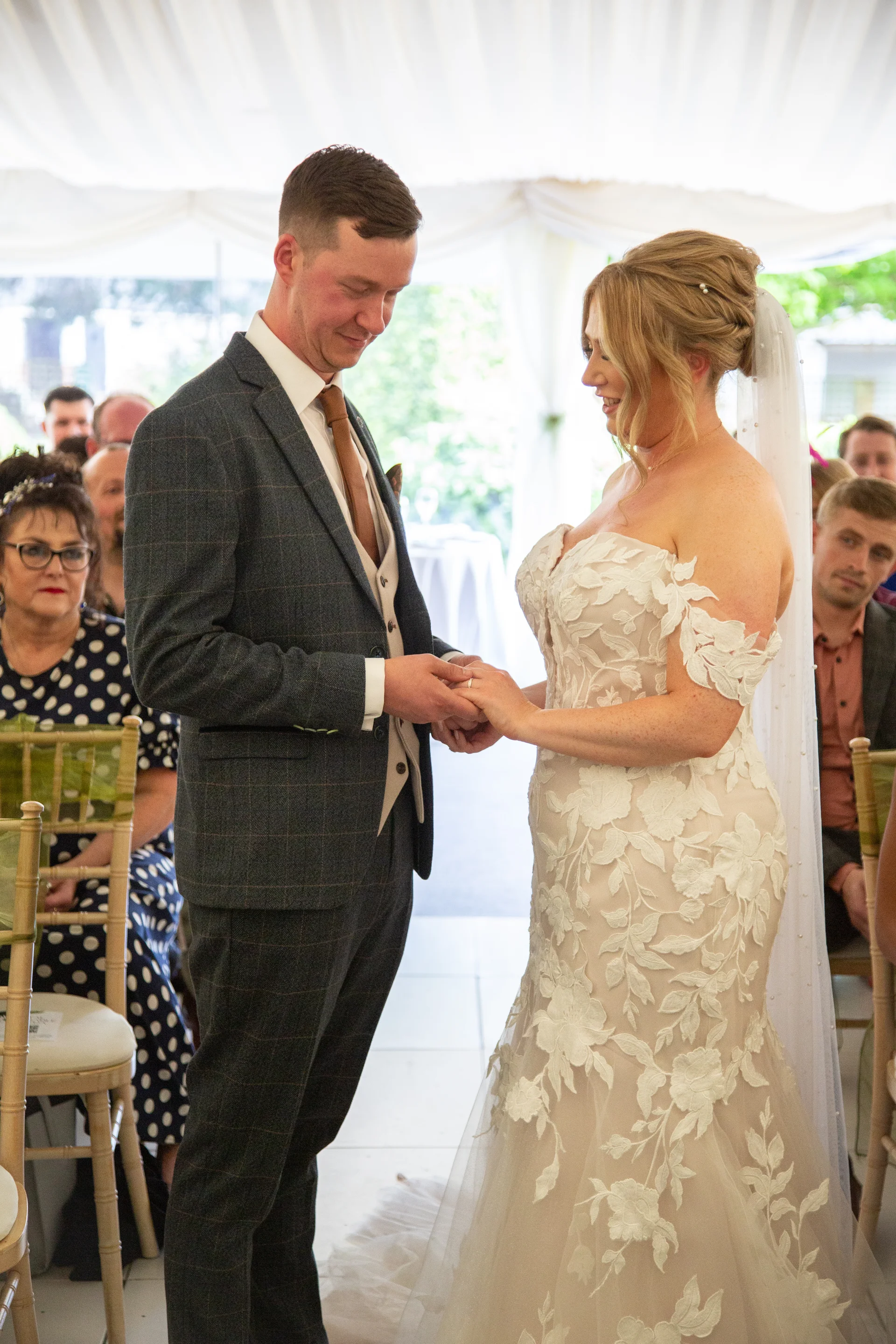 The groom gently slips a ring onto the bride's finger during their heartfelt ceremony inside a bright marquee.
