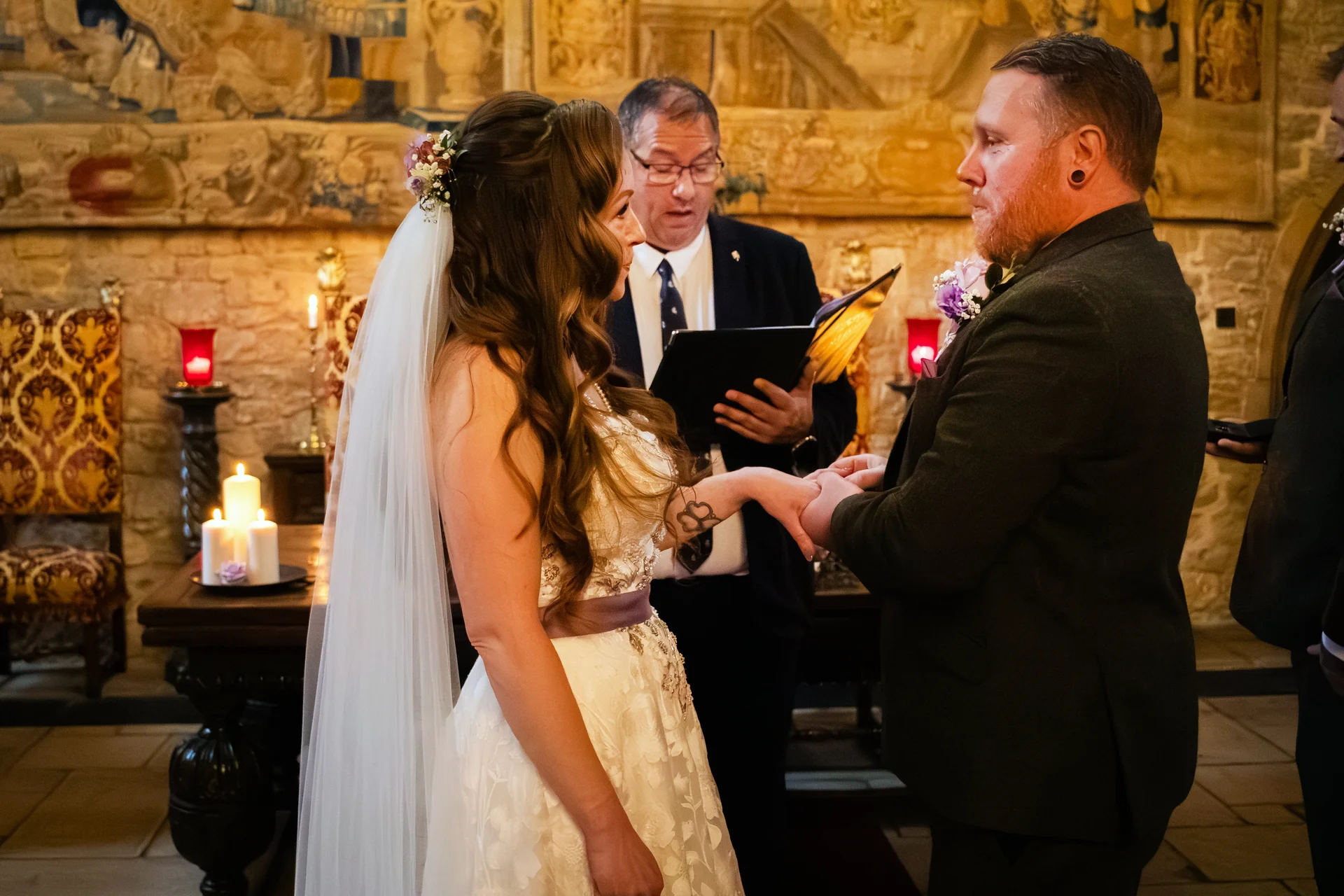 A bride and groom exchange rings during an intimate indoor civil ceremony inside a historic stone venue lit by candlelight.