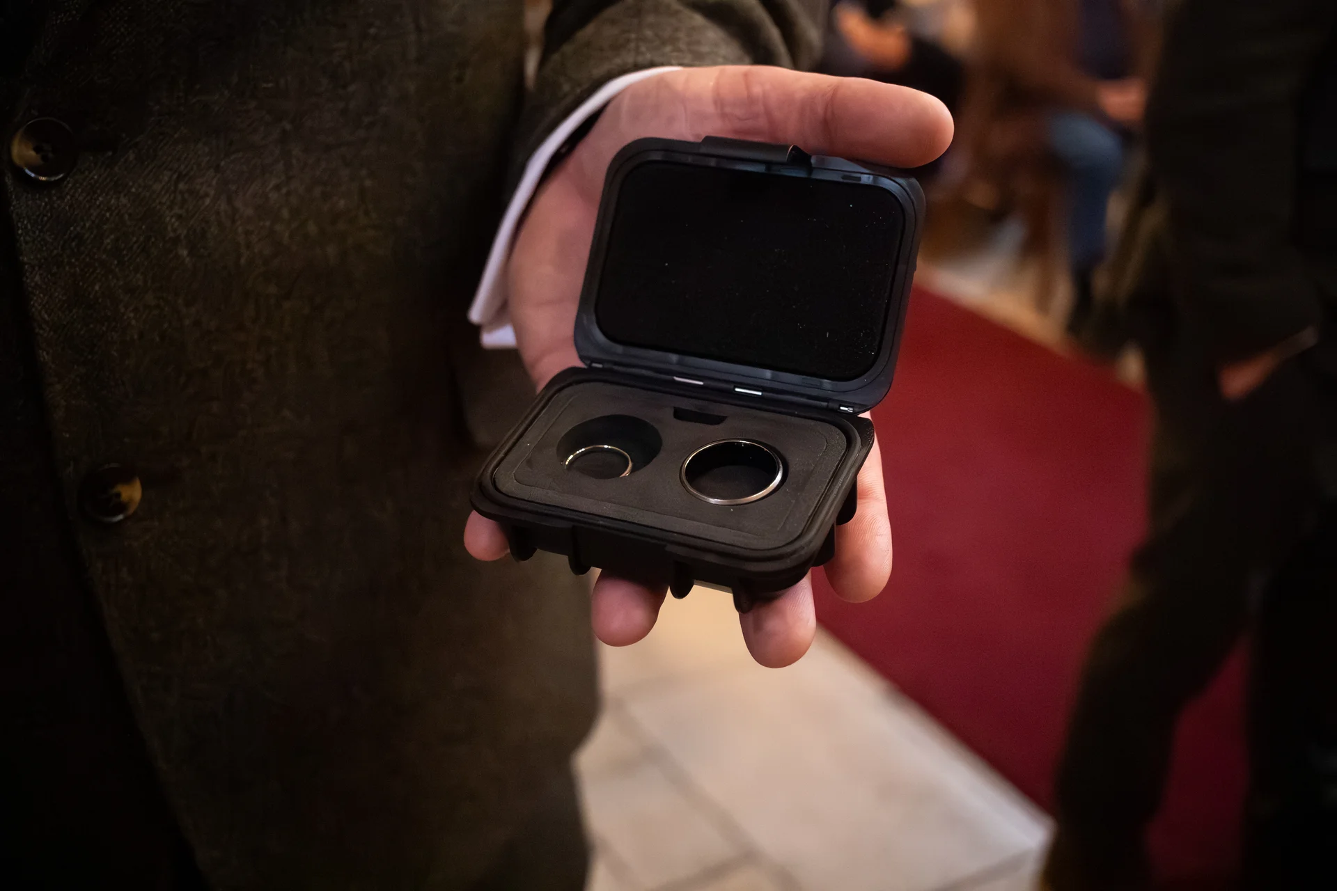 A close-up shot of a person holding an open black ring box containing two wedding bands during a ceremony.