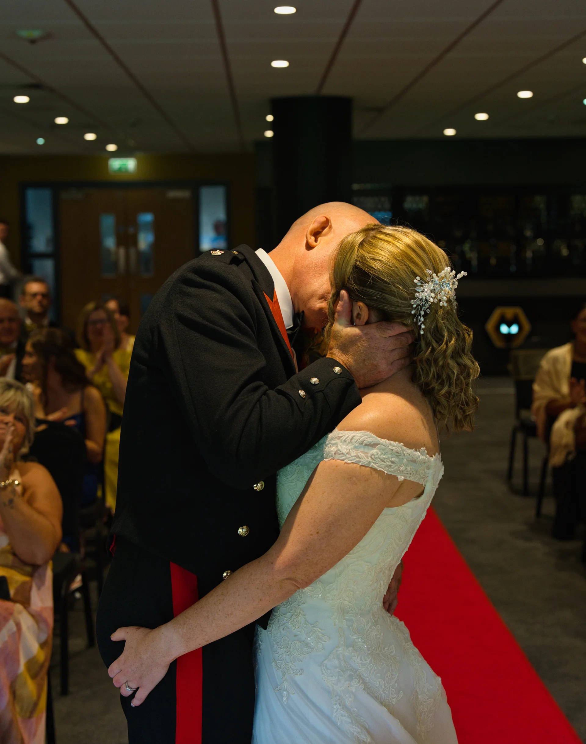 A newlywed couple share their first kiss at the altar, with the groom dressed in a military uniform and the bride wearing an off-the-shoulder lace gown.