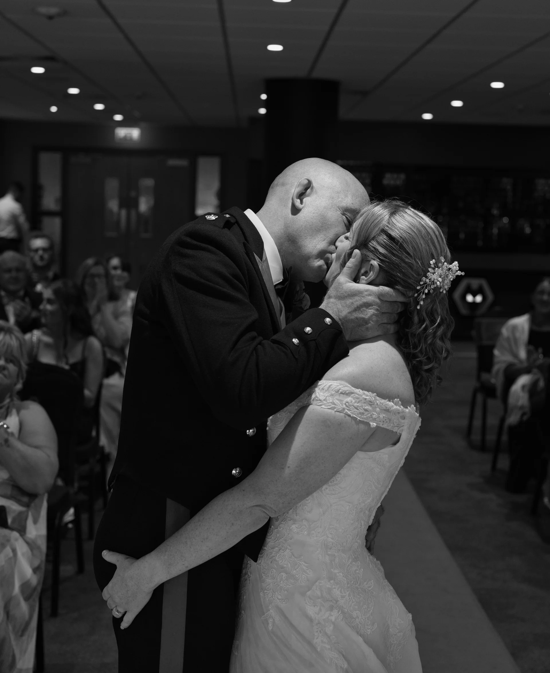A newlywed couple shares their first kiss as husband and wife during the ceremony while wedding guests look on.
