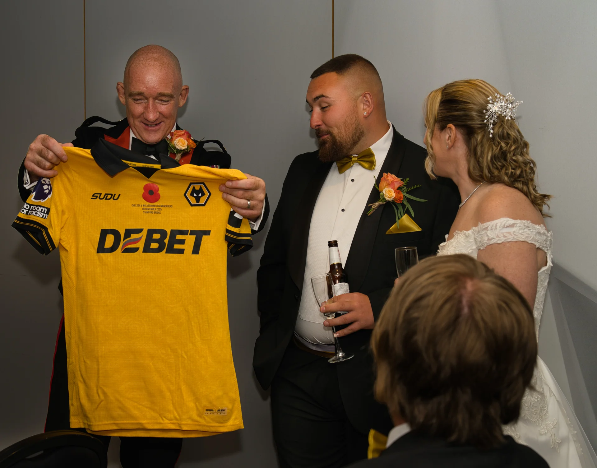 A guest holds up a football shirt with a personalized print during the wedding speeches while the groom and bride look on and smile.
