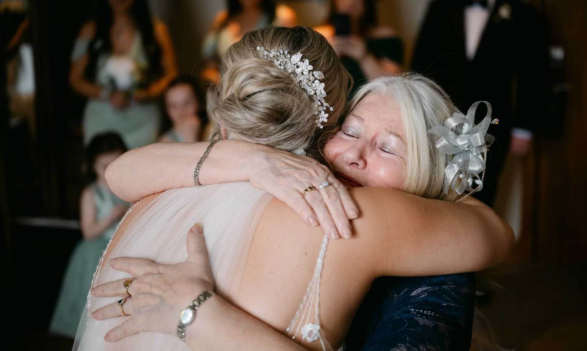 An emotional mother of the bride shares a tearful embrace and tender hug with the bride, showcasing a sparkling hair comb and close-up moment.