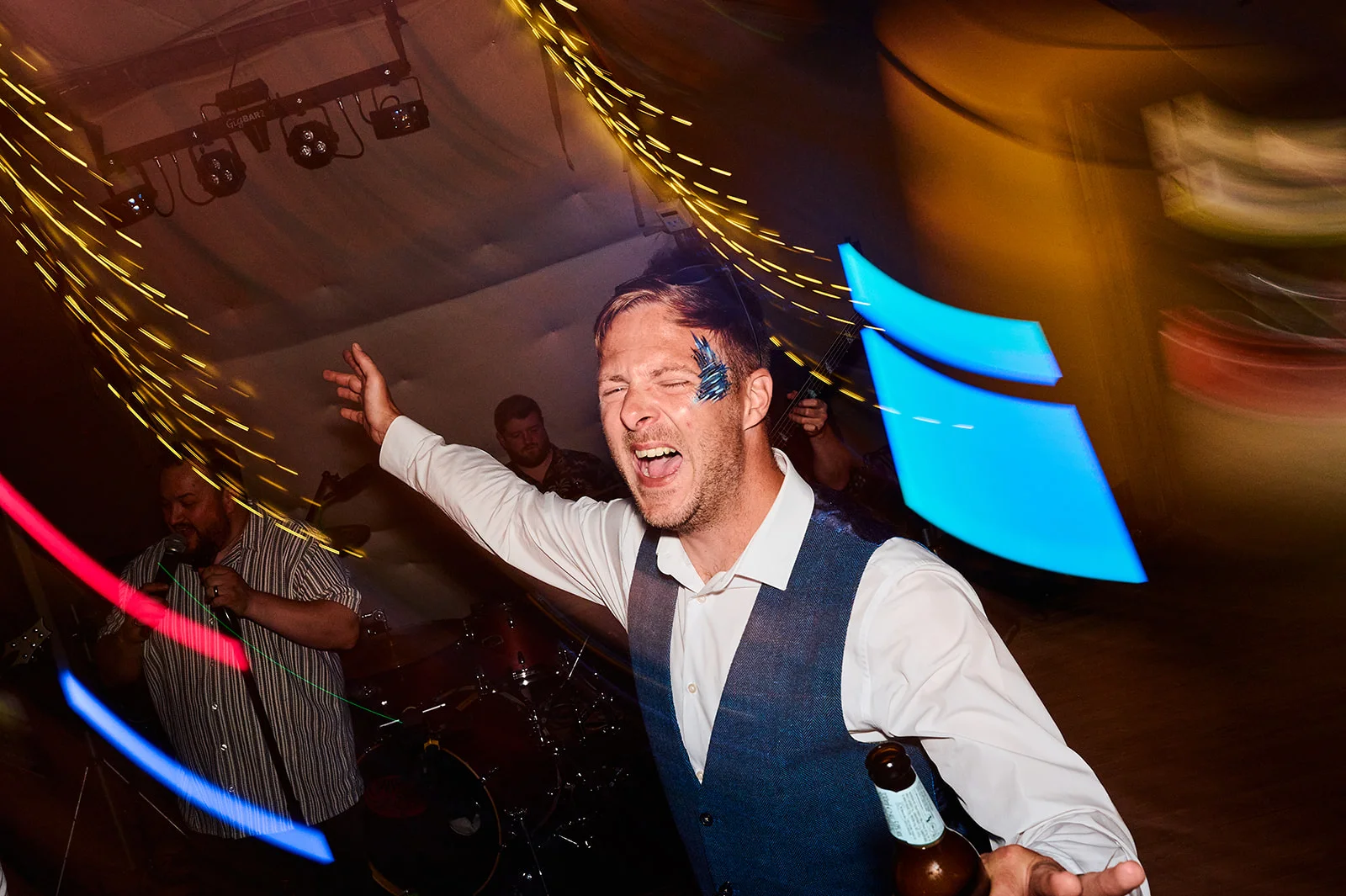 A guest dancing energetically on a wedding dance floor with dynamic motion blur, dramatic stage lights, and a live band performing in the background.