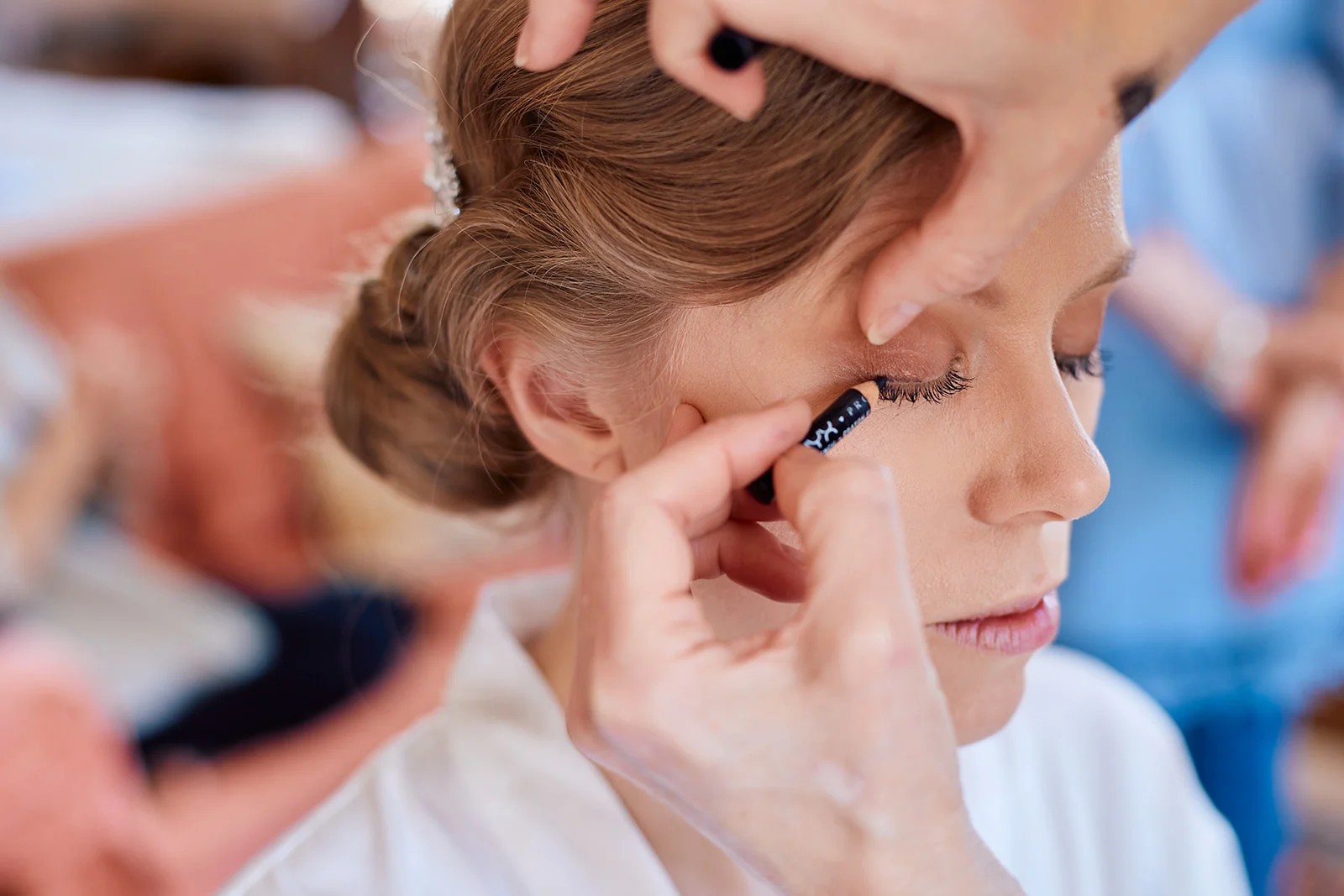 A close-up shot captures a makeup artist meticulously applying eyeliner to the bride's eye during morning bridal preparations.