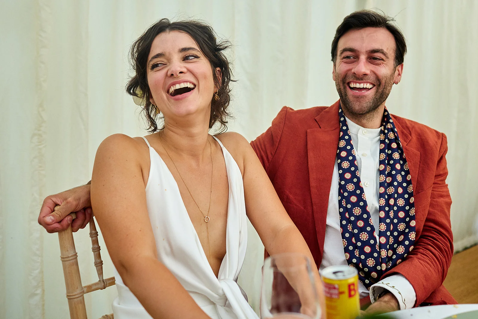 A newlywed couple shares a joyful, laughing moment together seated at a wedding reception.
