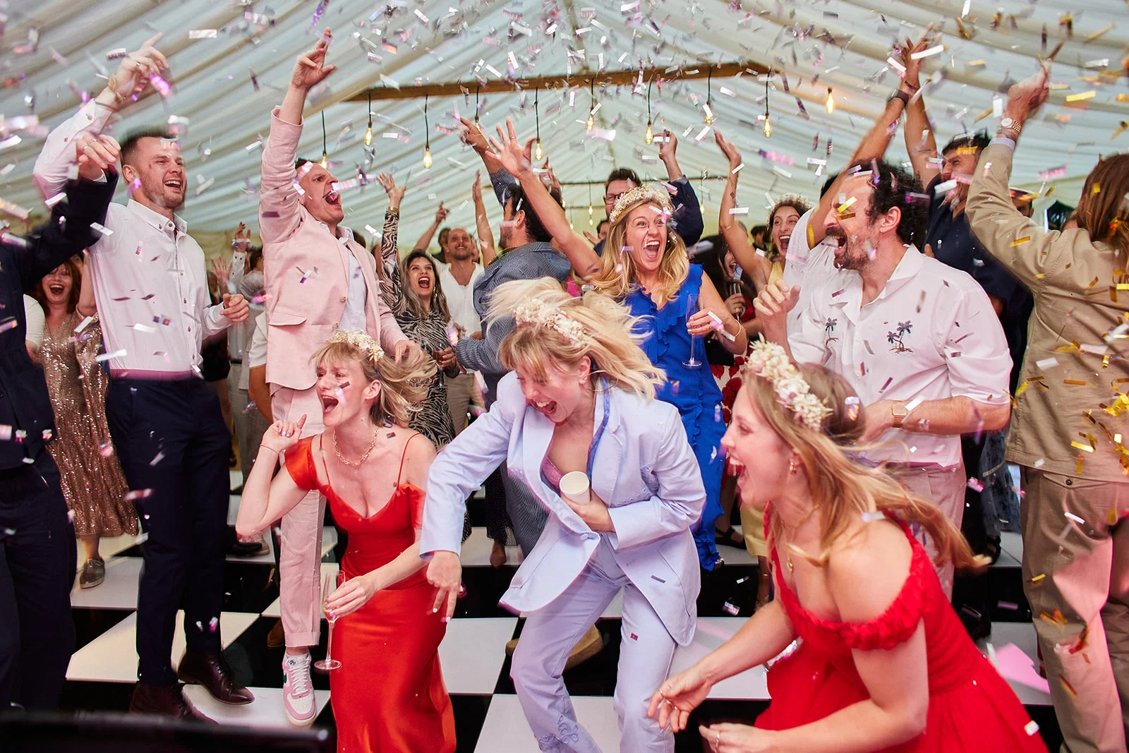 An exuberant crowd of wedding guests dances wildly under a marquee as metallic confetti rains down around them.