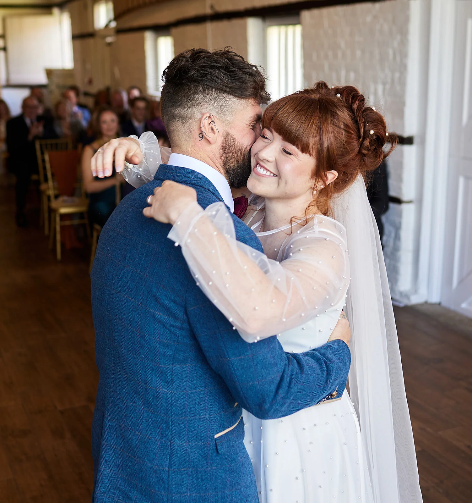A newlywed couple embraces and smiles happily during their indoor ceremony inside a rustic barn venue.